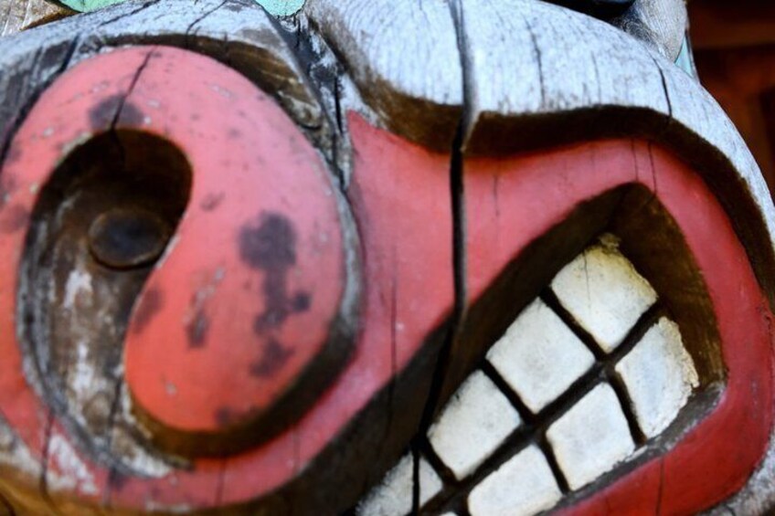A close-up of a wooden sculpture with a red and white face, a circular hole, and a grid pattern. 3