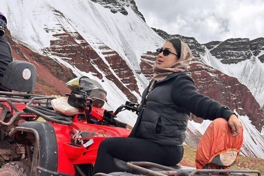 A person sitting on a red ATV in a mountainous area with snow-covered peaks. 1