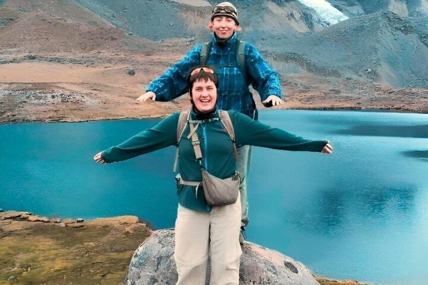 Two people standing on a rock with a lake and mountains in the background. 2