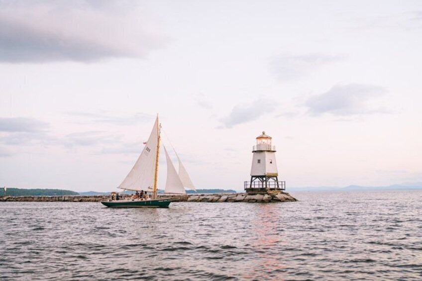 A sailboat with a white sail and a lighthouse on a rocky outcrop. 5