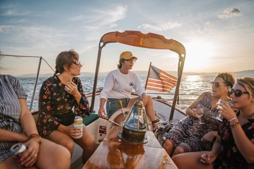 A group of people on a boat with an American flag, a steering wheel, and a table with drinks. 2