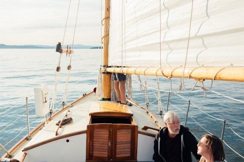 A sailboat with a person standing at the stern and two others seated at the bow. 5