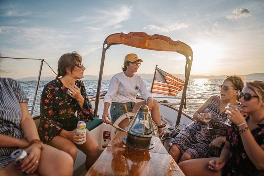 A group of people on a boat with a wooden canopy, a flag, and a sunset in the background. 2