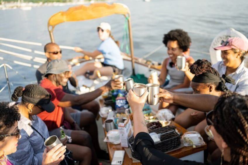 A group of people on a boat, holding mugs, and toasting. 4
