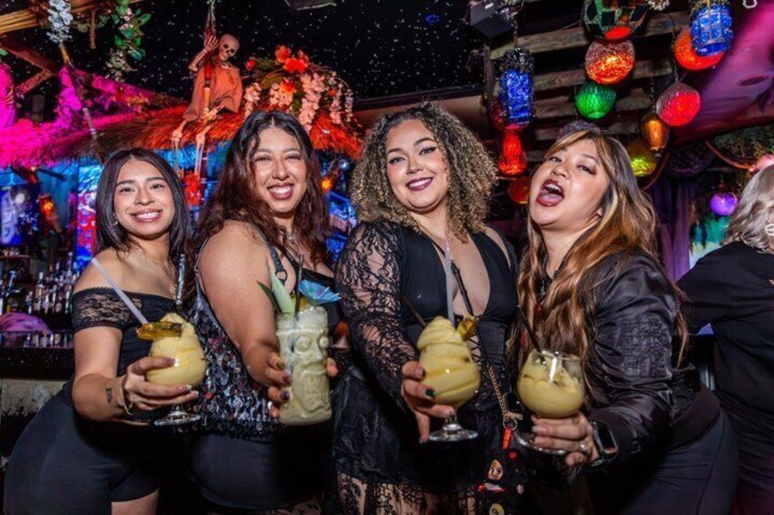 A group of people holding drinks at a festive event with colorful decorations and a wooden structure in the background. 3