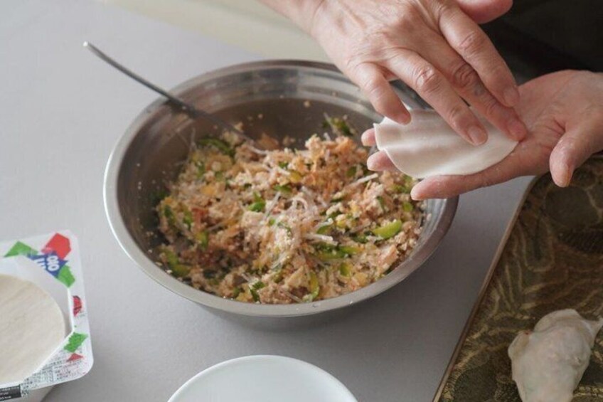 A person preparing food, with a bowl of salad and a dumpling wrapper on the table. 4