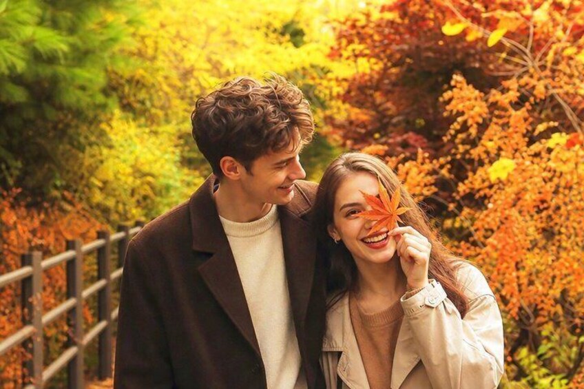 Two people standing on a wooden bridge surrounded by autumn foliage. 1
