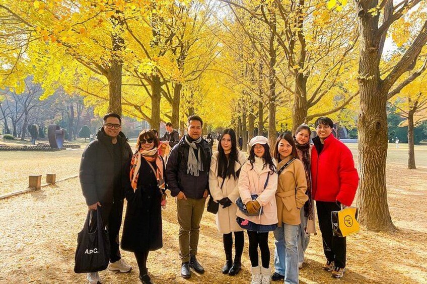 A group of people standing under yellow-leaved trees in a park. 2