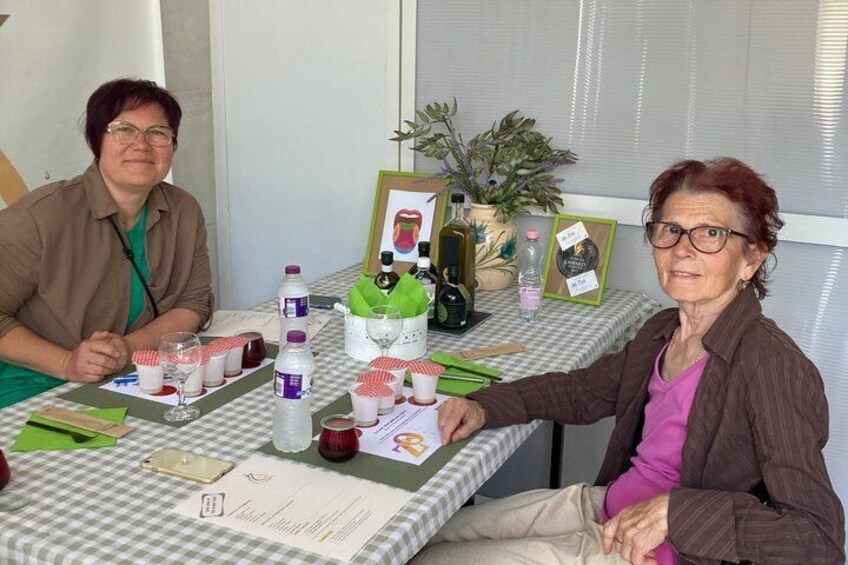 Two people seated at a table with a checkered tablecloth, various bottles, glasses, and a framed picture. 3