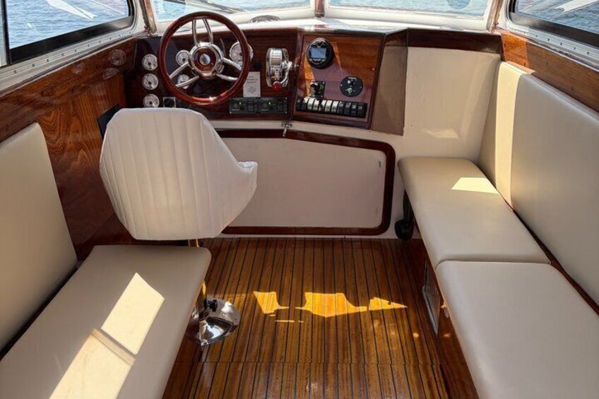 A boat's interior with a steering wheel, control panel, and cushioned seating. 2