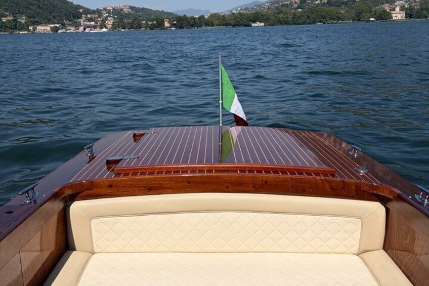 A boat with a wooden deck and a flag, on a calm lake with a distant shoreline. 4
