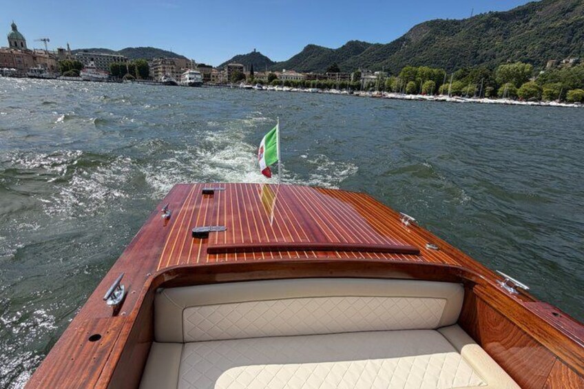 A wooden boat with a flag, moving on a river with a cityscape in the background. 1
