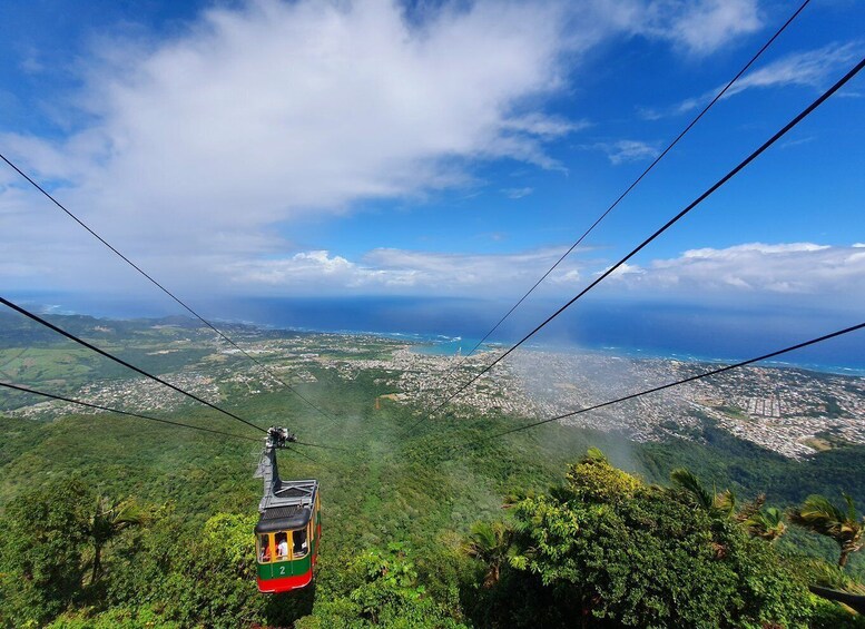 A cable car moving through lush green hills with a cityscape in the background. 2