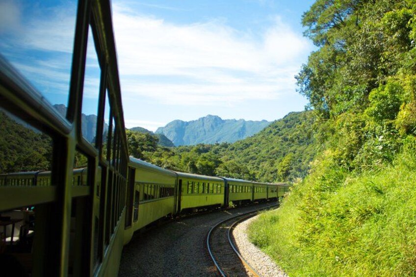 A train traveling through a lush, green landscape with mountains in the background. 5
