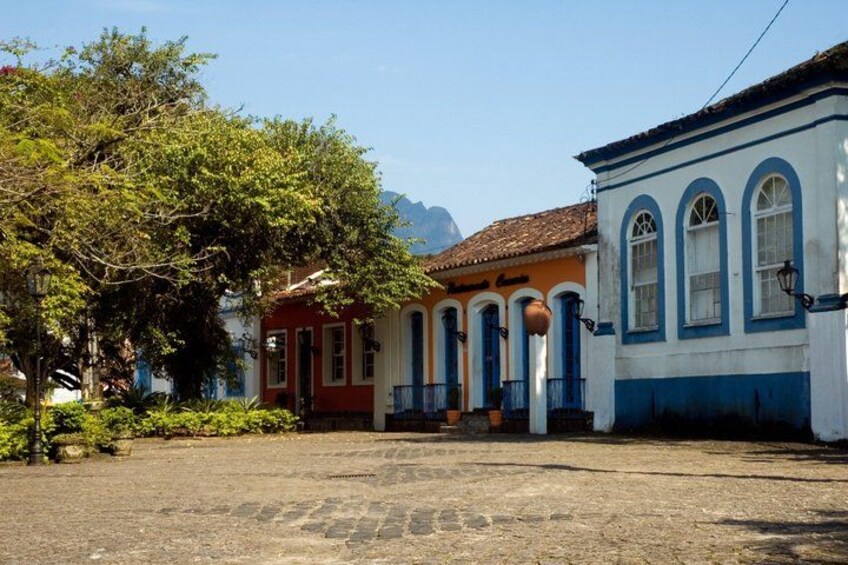 A colonial-style building with arched windows and a red door, surrounded by lush greenery and cobblestone ground. 3