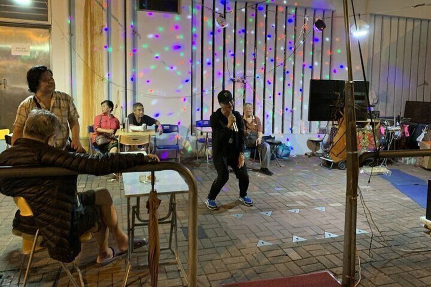 A group of people sitting at tables, a person walking, and a stage with musical instruments. 3