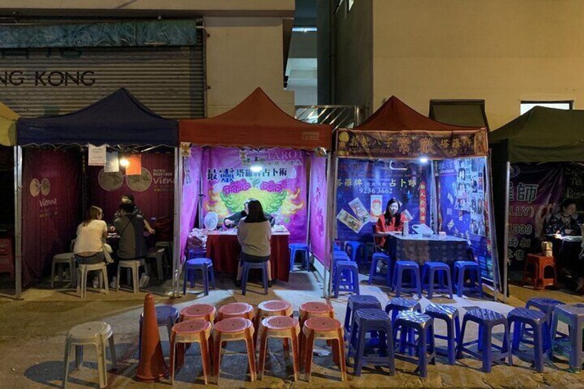 A food stall with a purple and orange canopy, surrounded by plastic chairs and tables. 4