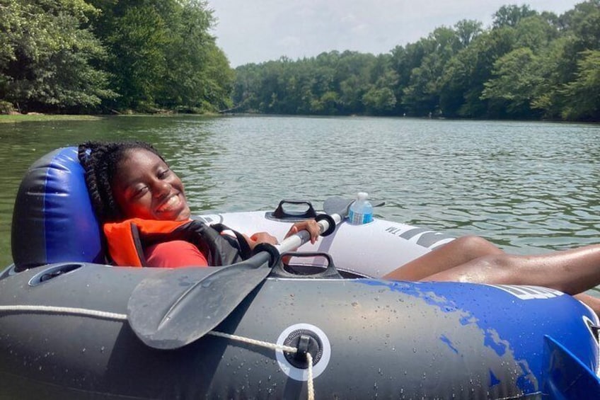 A person in a raft on a calm body of water surrounded by trees. 4