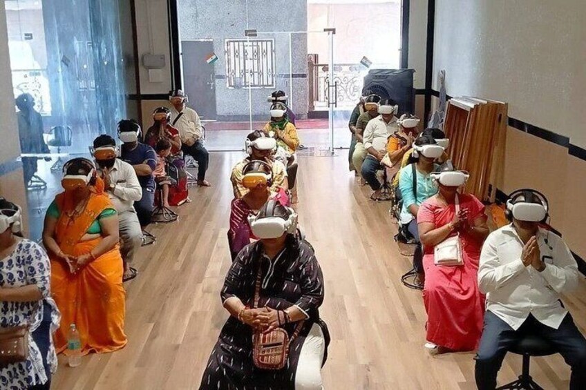 A group of people seated in a room with a wooden floor, some wearing headsets. 5