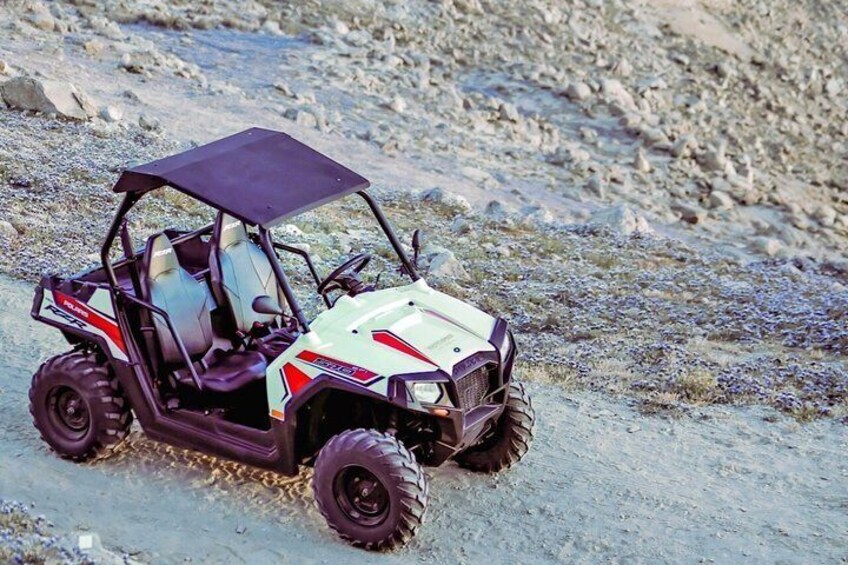 A white and red off-road vehicle with a black roof on a rocky terrain. 1