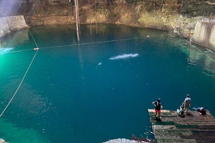 A clear blue pool with a wooden dock and people standing on it. 2