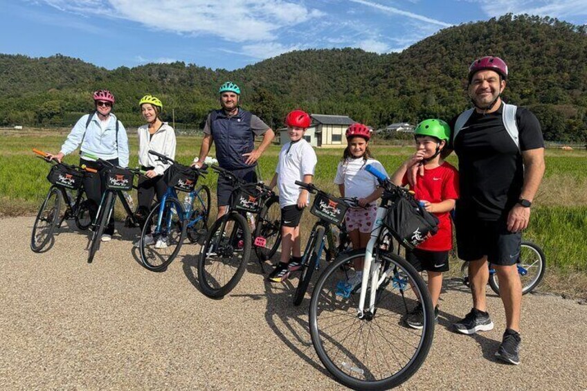 A group of people with bicycles on a paved path with a rural landscape in the background. 1