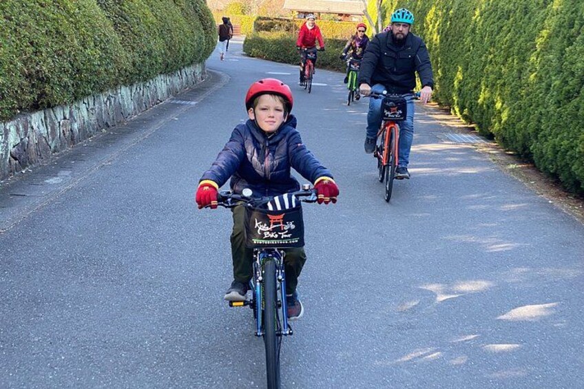 A child riding a bicycle on a paved path with greenery on both sides. 4