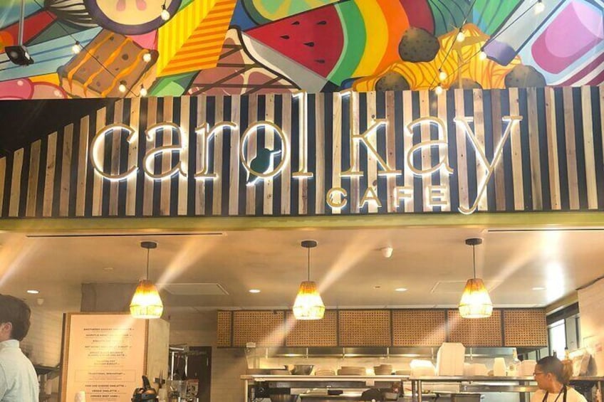 A cafe with a colorful, fruit-themed ceiling and a neon sign that reads 'carol hay cafe.' 5
