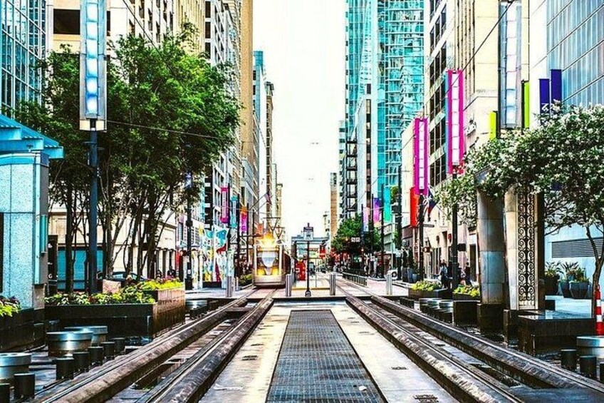 A city street with tram tracks, buildings, and trees. 3