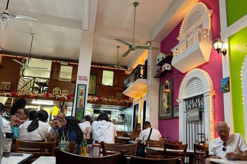 Un restaurante animado con muebles de madera, pared verde y rosa, y luces decorativas. 2