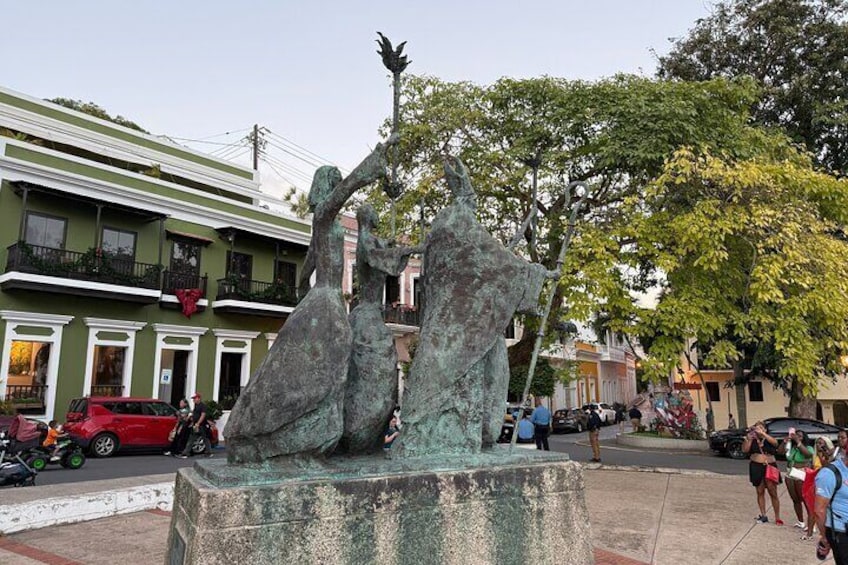 A bronze sculpture of two figures in a public square with buildings in the background. 2