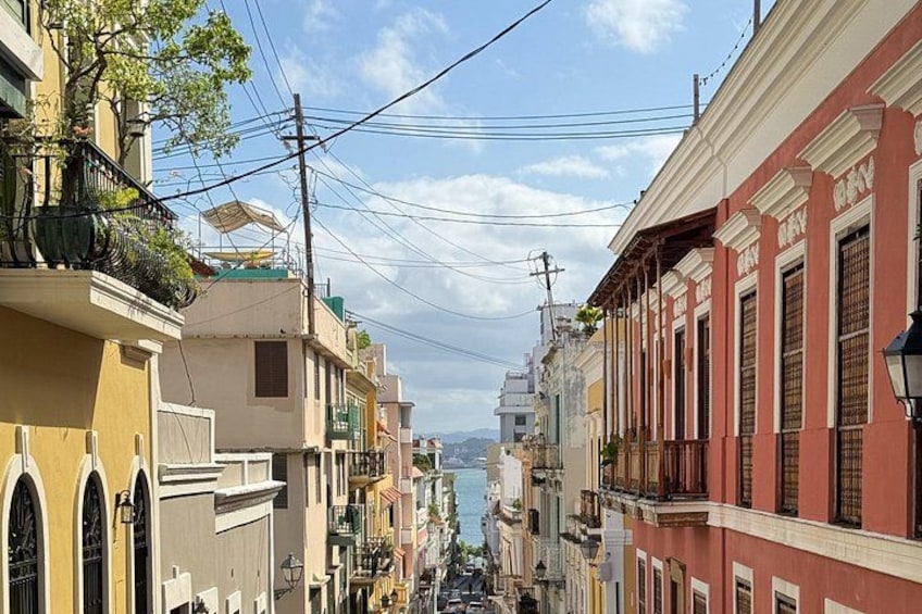 A narrow street lined with colorful buildings, a clear sky, and power lines. 3