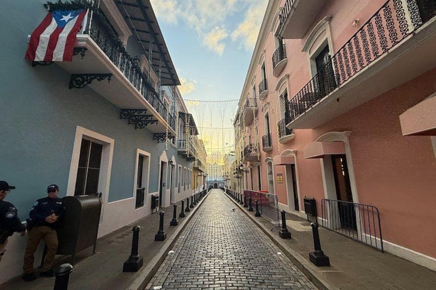 A cobblestone street lined with pastel-colored buildings, a flag, and a police officer. 2
