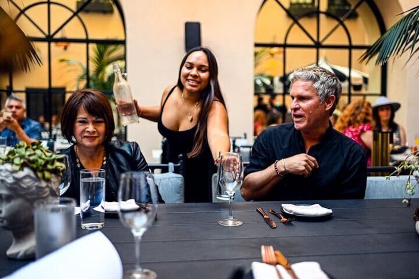 A group of people dining at an outdoor restaurant with a black tablecloth, wine glasses, and a bottle of champagne. 1