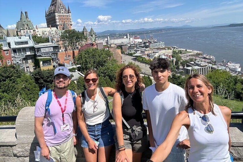 A group of people standing on a viewing platform overlooking a cityscape with a prominent tower and waterfront. 1