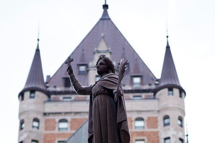 A statue of a person with a cross, in front of a building with a pointed roof and two towers. 2