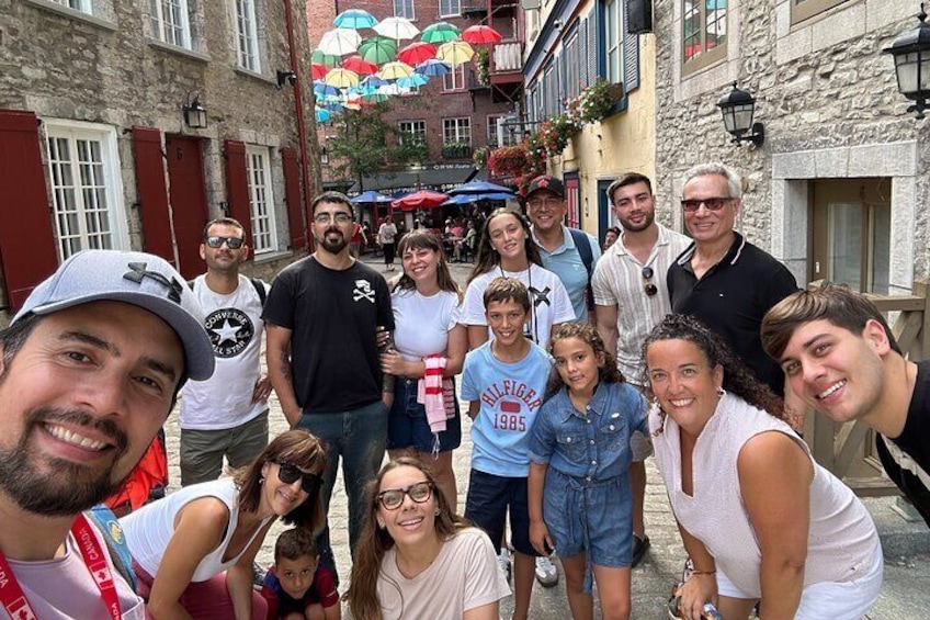 A group of people posing in a narrow street with stone buildings and colorful umbrellas in the background. 3