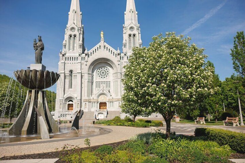 A grand cathedral with twin spires, a central rose window, and a fountain with a statue. 1