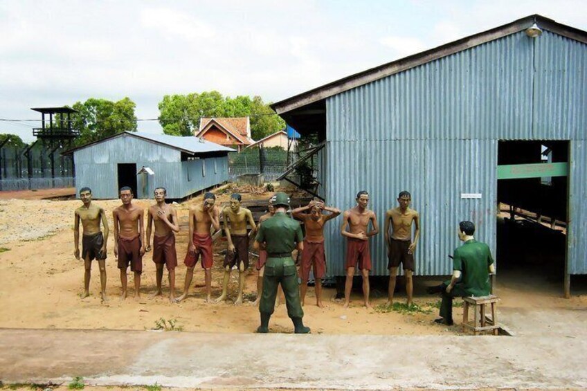 A group of shirtless men standing in a dirt area with a blue building in the background. 3