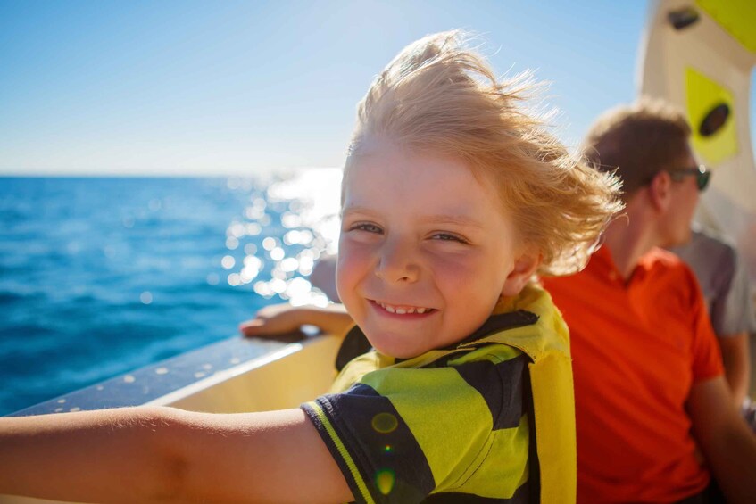 A person wearing a life jacket on a boat with the ocean in the background. 3