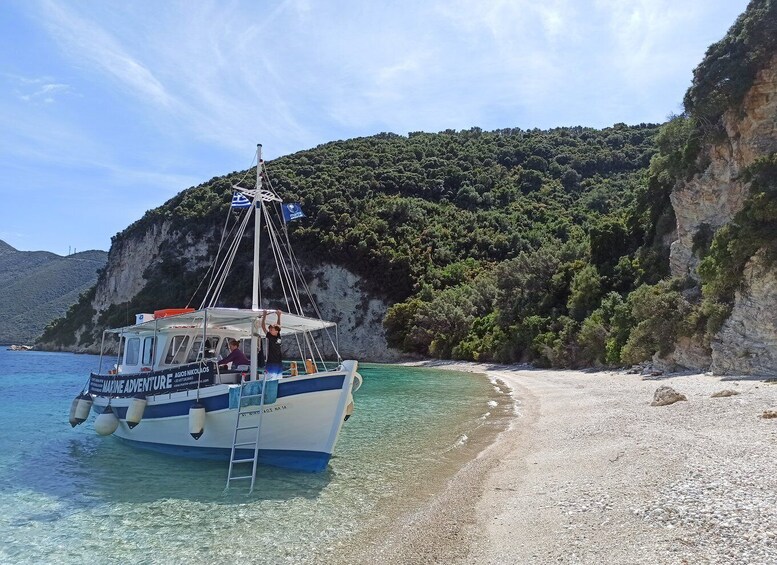 A boat named 'Marine Adventure' anchored near a rocky beach with clear turquoise water and a backdrop of lush green hills. 2