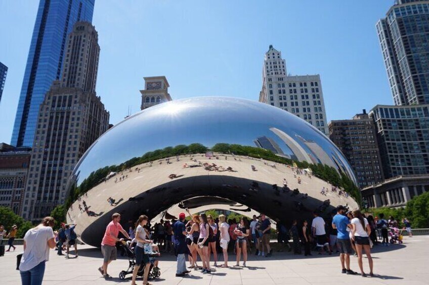 A large reflective sculpture surrounded by people, with modern buildings in the background. 3