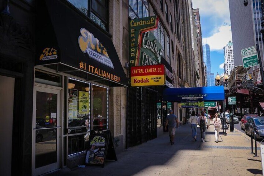 A street with Italian Beef and Central Camera Co. signs, pedestrians, and urban buildings. 2