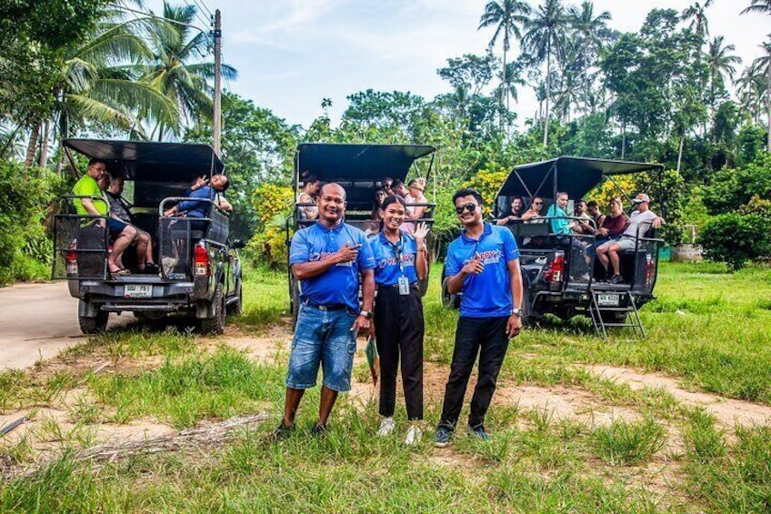 Three people standing in front of a jeepney with passengers, surrounded by greenery and palm trees. 2