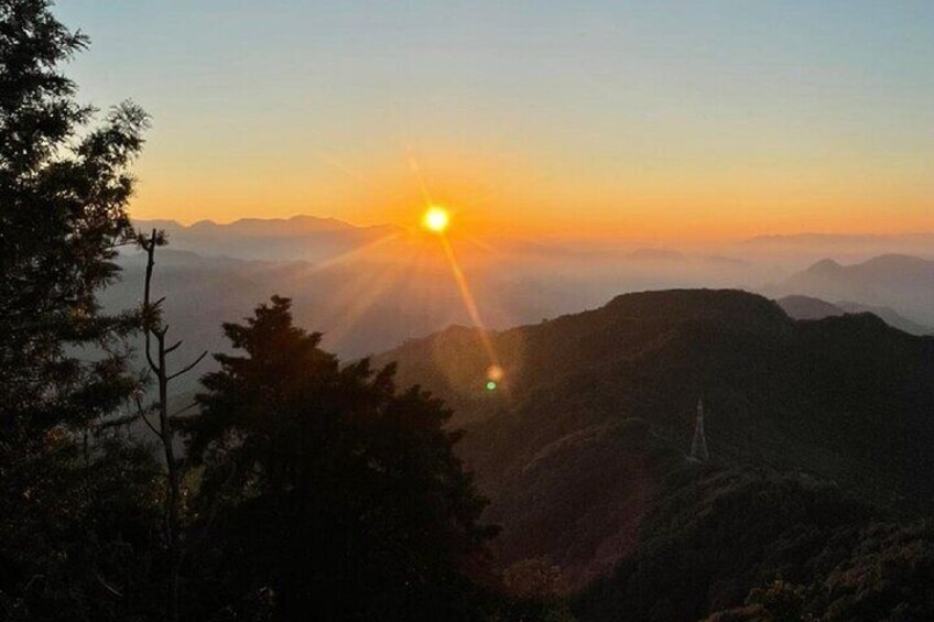 A mountain landscape at sunrise with the sun visible above the horizon. 1