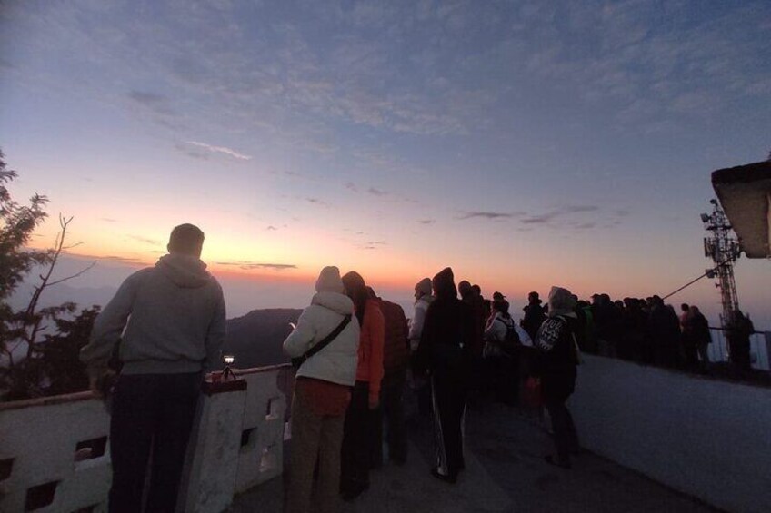 A group of people standing on a viewing platform overlooking a sunset. 2
