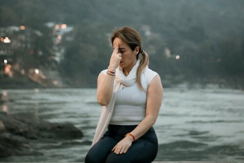 A person sitting by a body of water with a rocky shoreline and buildings in the background. 1