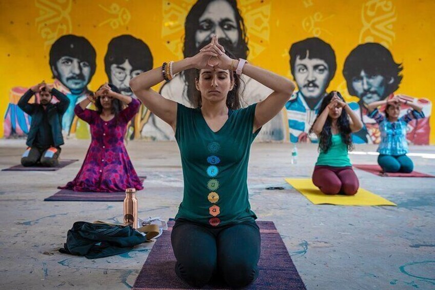 A group of people performing yoga on mats in an outdoor setting with a colorful mural in the background. 5