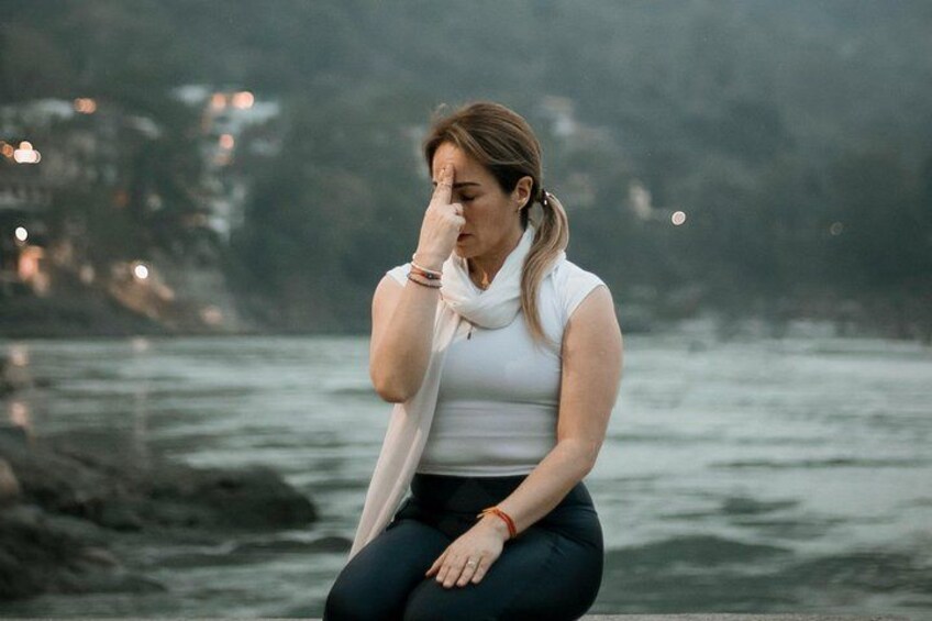 A person sitting by a body of water with a rocky shoreline and buildings in the background. 1
