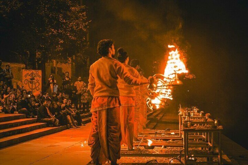 A nighttime outdoor event with a fire ritual, an audience, and a stage with musical instruments. 3